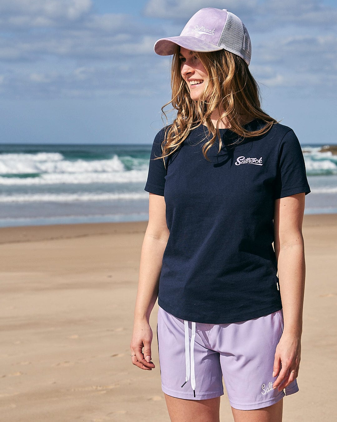 A woman is standing on the beach wearing a Saltrock Trademark Womens Short Sleeve T-Shirt in Navy and shorts.
