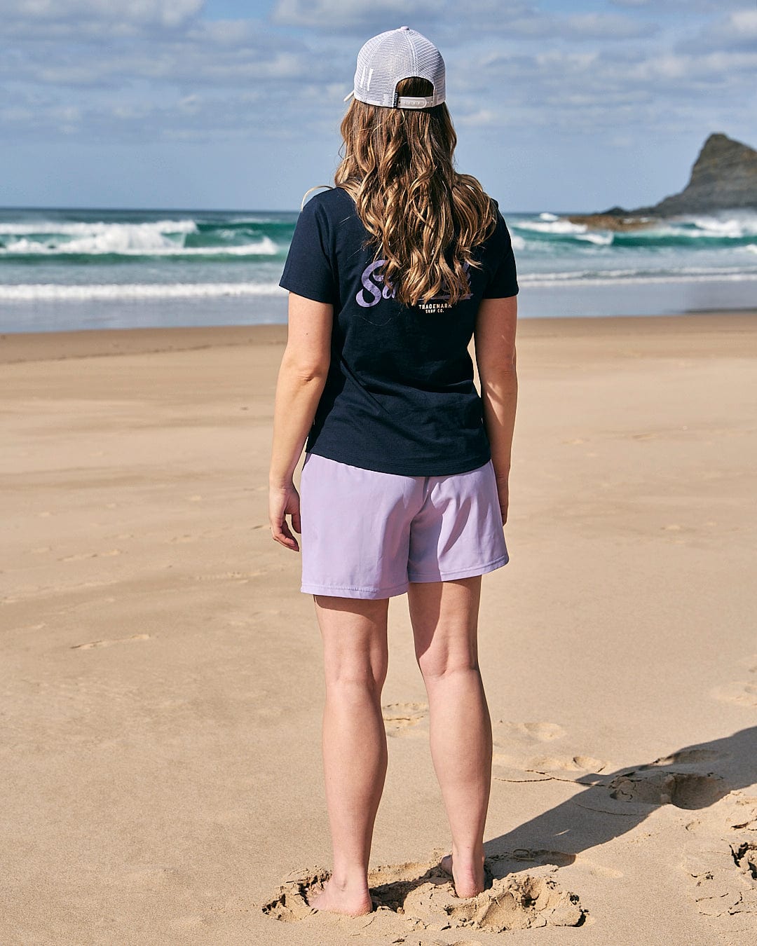 A woman standing on the beach wearing a Saltrock womens short sleeve t-shirt in navy and shorts.