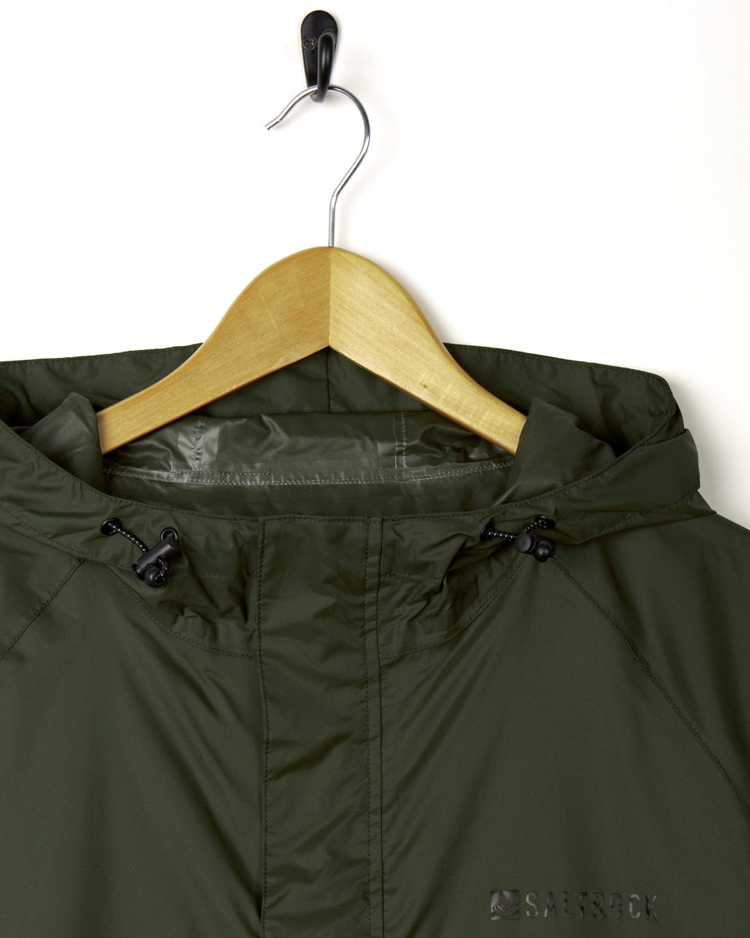 Green Rainier - Mens Packable Waterproof Jacket by Saltrock hanging on a wooden hanger against a white background, detailed view of the collar and upper part.