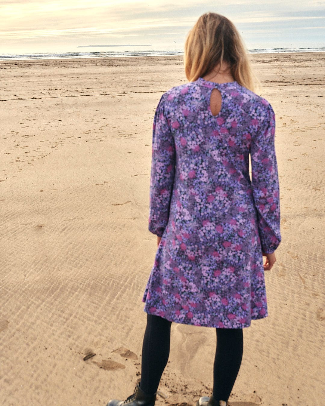 A woman is standing on the beach in a Saltrock Ramona Womens Mock Jersey Dress - Purple.