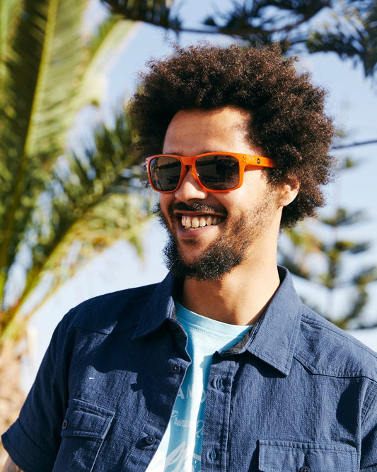Man with curly hair wearing Saltrock Ranger - Recycled Polarised Sunglasses - Orange and a blue shirt smiling outdoors.