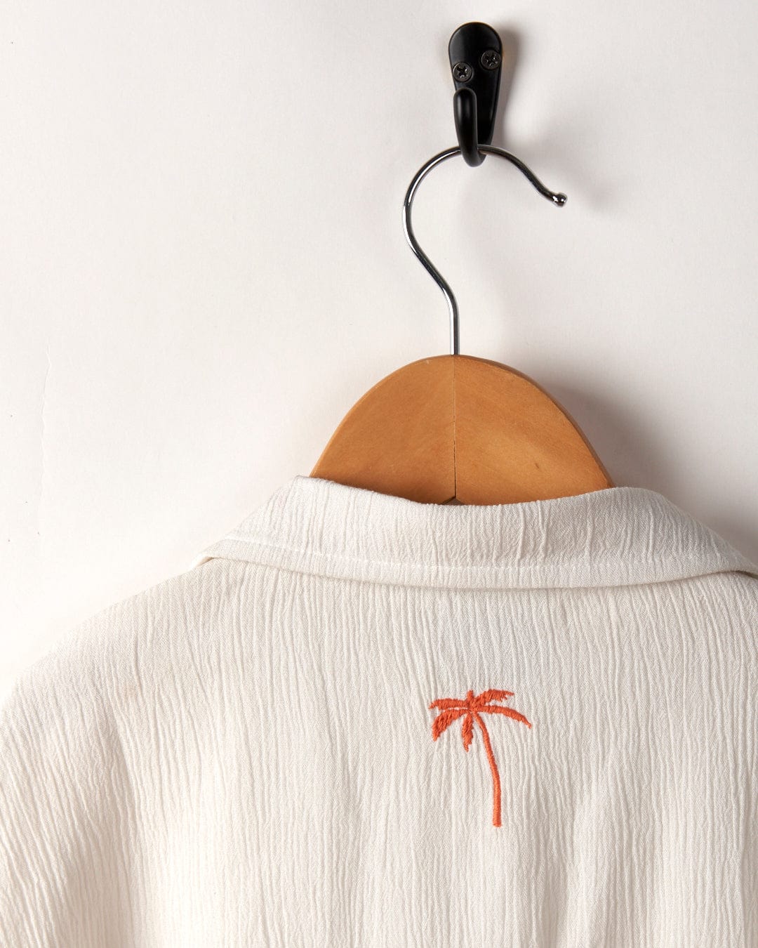 Orange Raya Kids Shirt from Saltrock hanging on a wooden hanger with a small palm tree embroidery on the back.