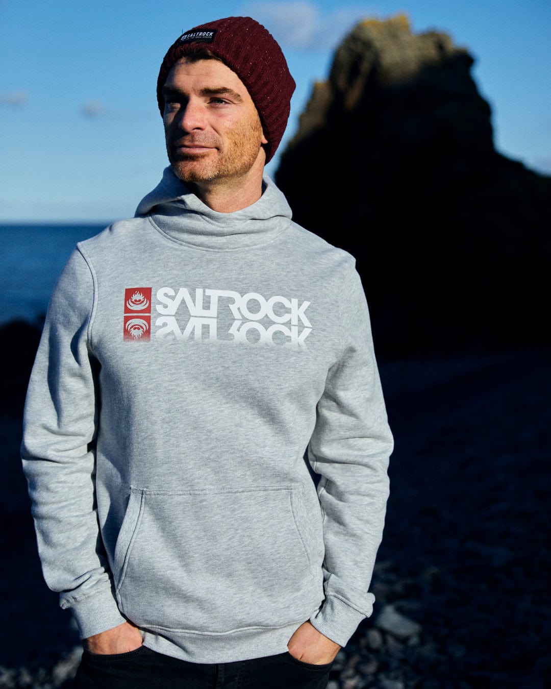 A man wearing a grey Reflect - Mens Pop Hoodie with the Saltrock branding on it.