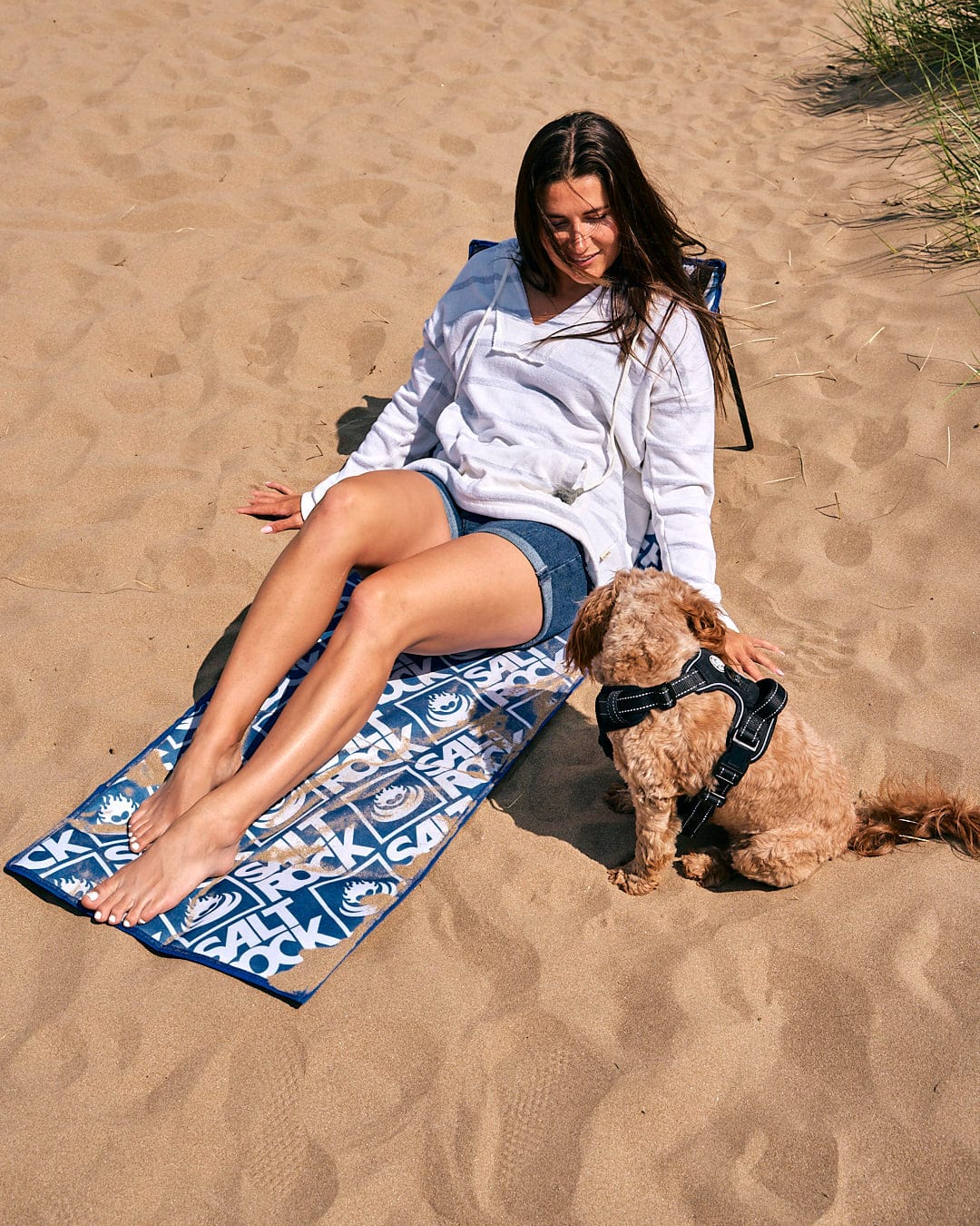 A woman lounging on a Saltrock Relax - Beach Mat - Blue with her dog.