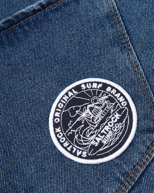 The pocket of a blue denim jacket has a Saltrock Retreat Patch - Navy on it.