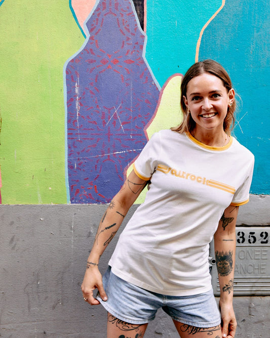 A woman in a Retro Ribbon - Womens Shorts Sleeve T-Shirt - White with Saltrock branding, smiling at the camera, standing in front of a colorful graffiti wall.