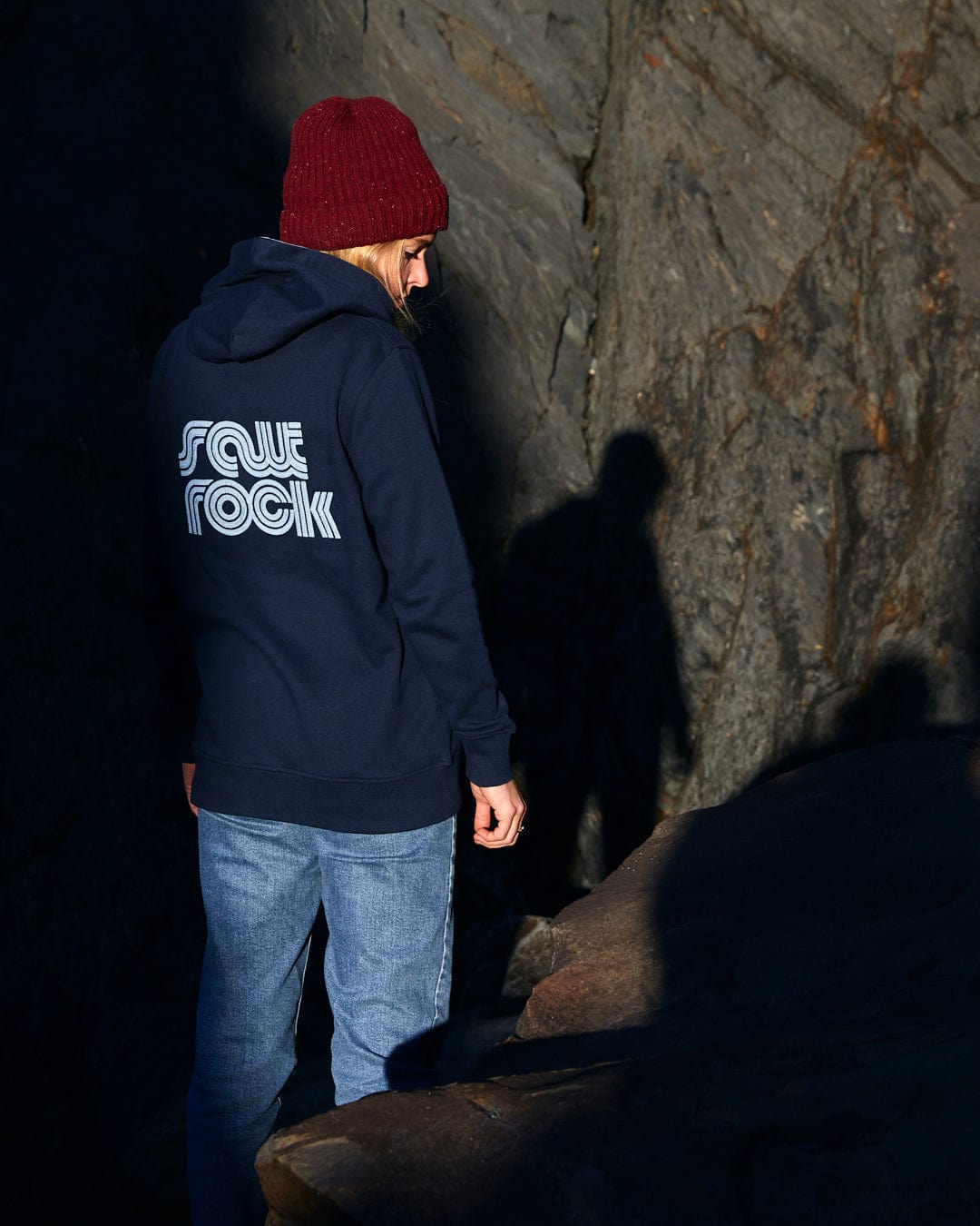 A person standing on a rock with a Saltrock Retro Wave Emb - Womens Zip Hoodie - Blue on, featuring front pockets and hood lining.