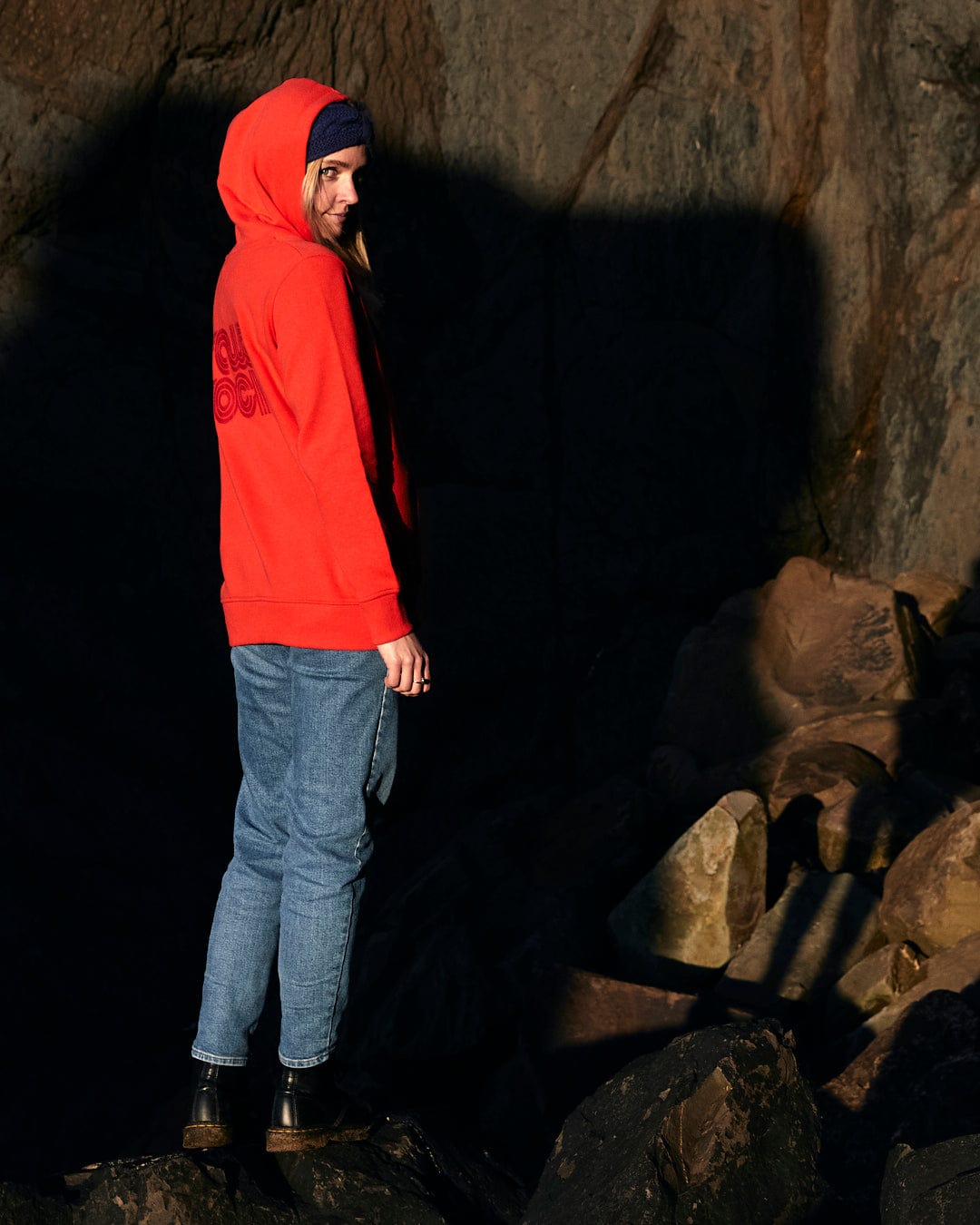 A woman in a red Retro Wave Embroidered - Womens Zip Hoodie - Red Saltrock hoodie standing on rocks with subtle Saltrock branding.
