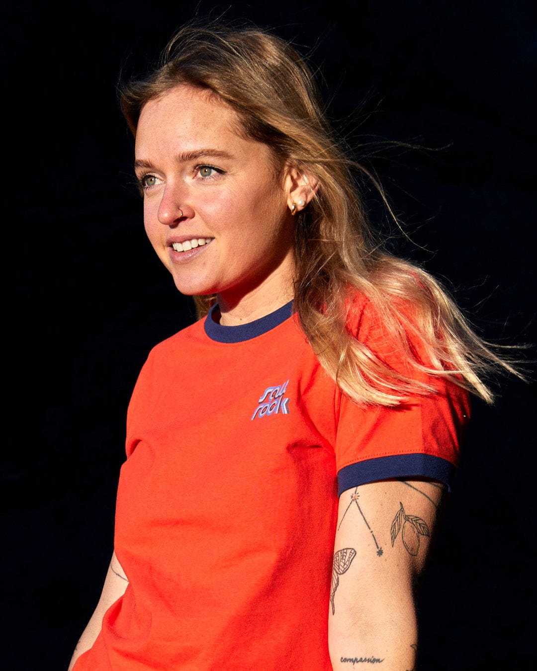 A woman in an orange t-shirt showcasing Saltrock branding with tattoos is wearing the Retro Wave Mini - Womens Short Sleeve T-Shirt in Red by Saltrock.