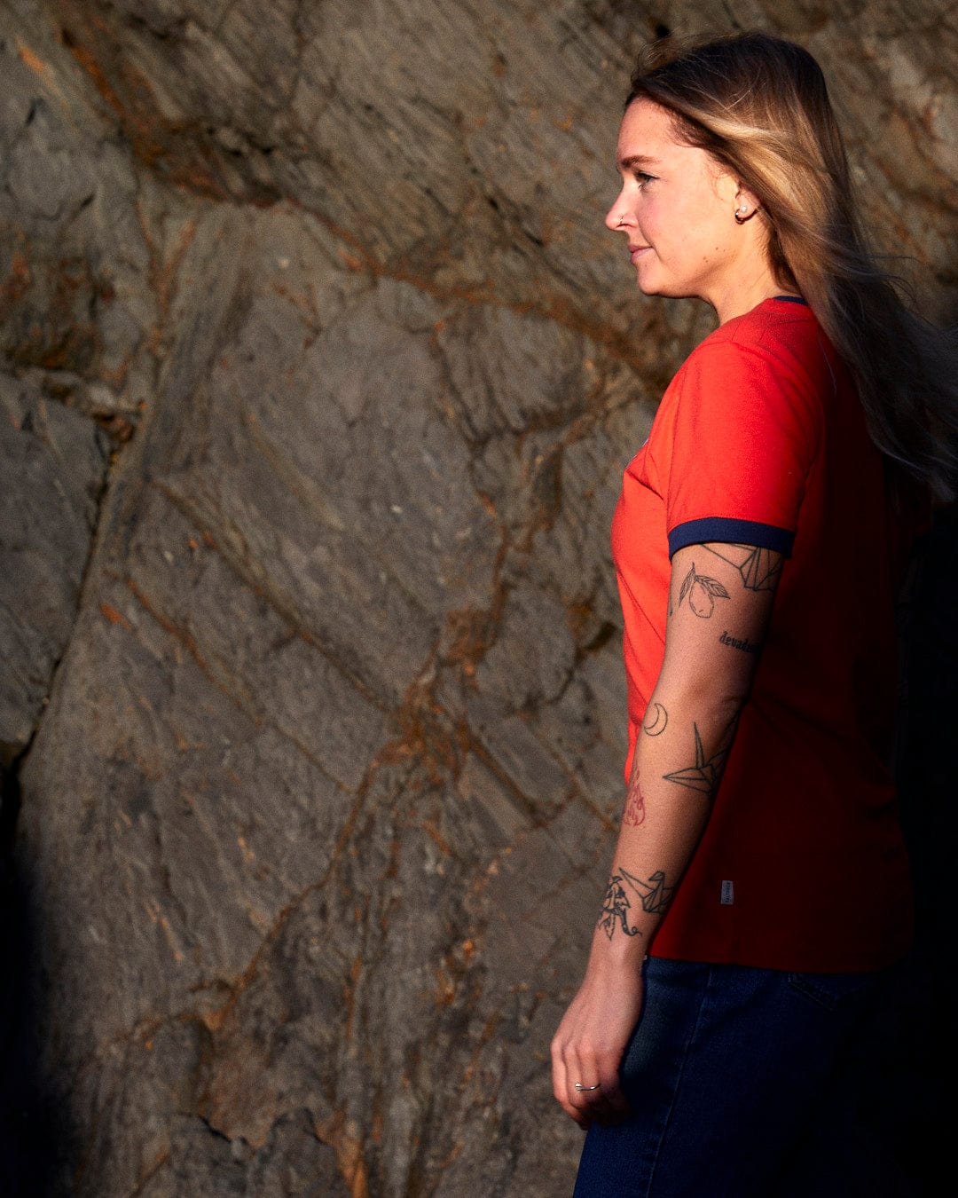A woman with Saltrock Retro Wave Mini - Womens Short Sleeve T-Shirt - Red branding tattoos standing next to a rock.