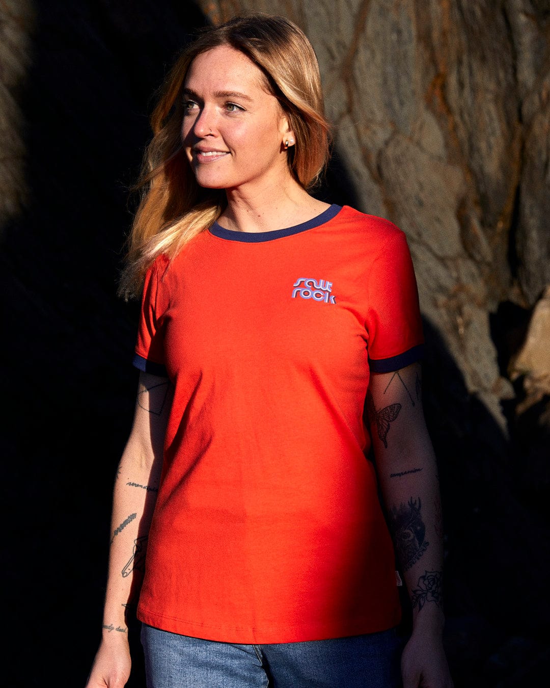 A woman wearing an Retro Wave Mini - Womens Short Sleeve T-Shirt - Red with Saltrock branding in front of rocks.