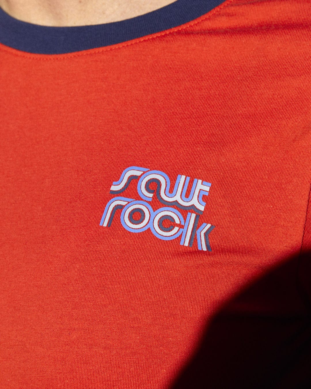 A man wearing a Retro Wave Mini red t-shirt with the Saltrock branding and the words "save rock" on it.