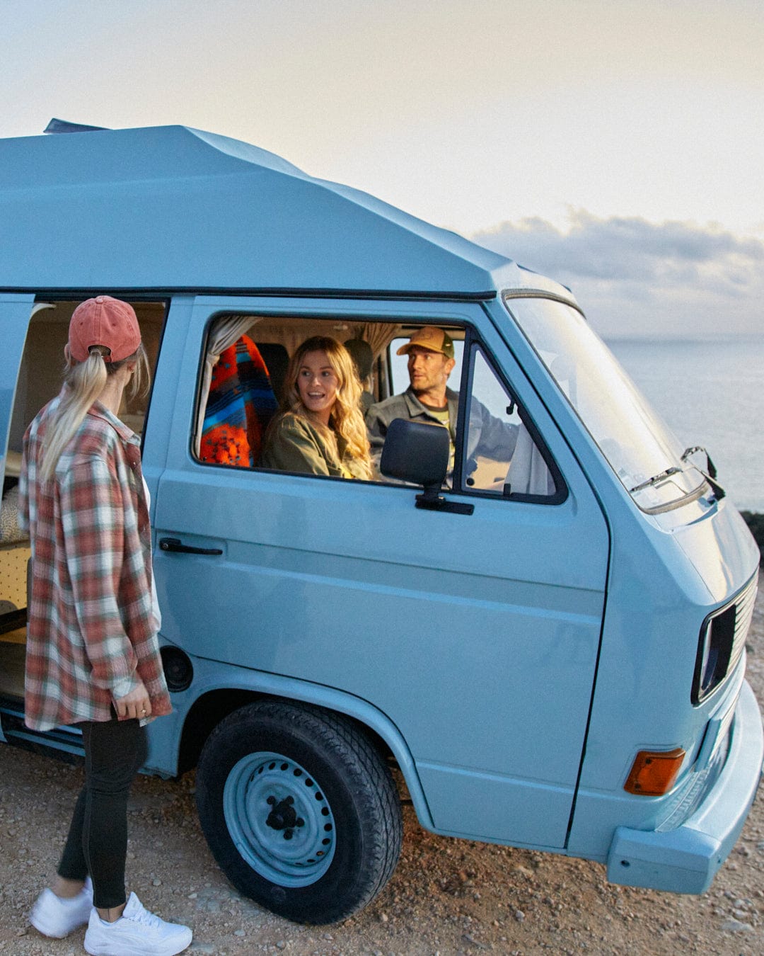 A group of people standing next to a blue VW camper van with a Saltrock Reversible Sherpa Lined Car Seat Cover - Green/Aztec.