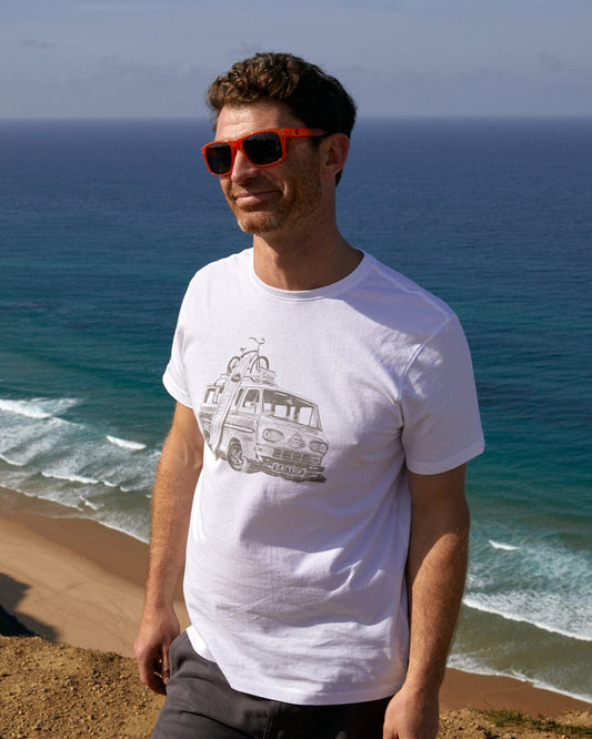 A man wearing a Saltrock Re-Wild - Mens Short Sleeve T-Shirt in White standing on a hill overlooking the ocean.