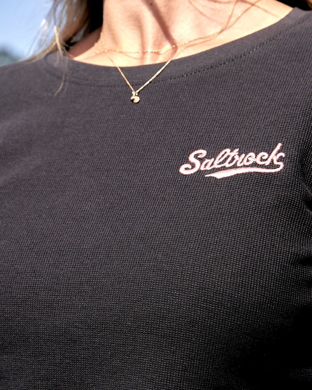 A woman wearing a Saltrock Rory - Womens Long Sleeve Waffle T-Shirt - Black with a pink logo.