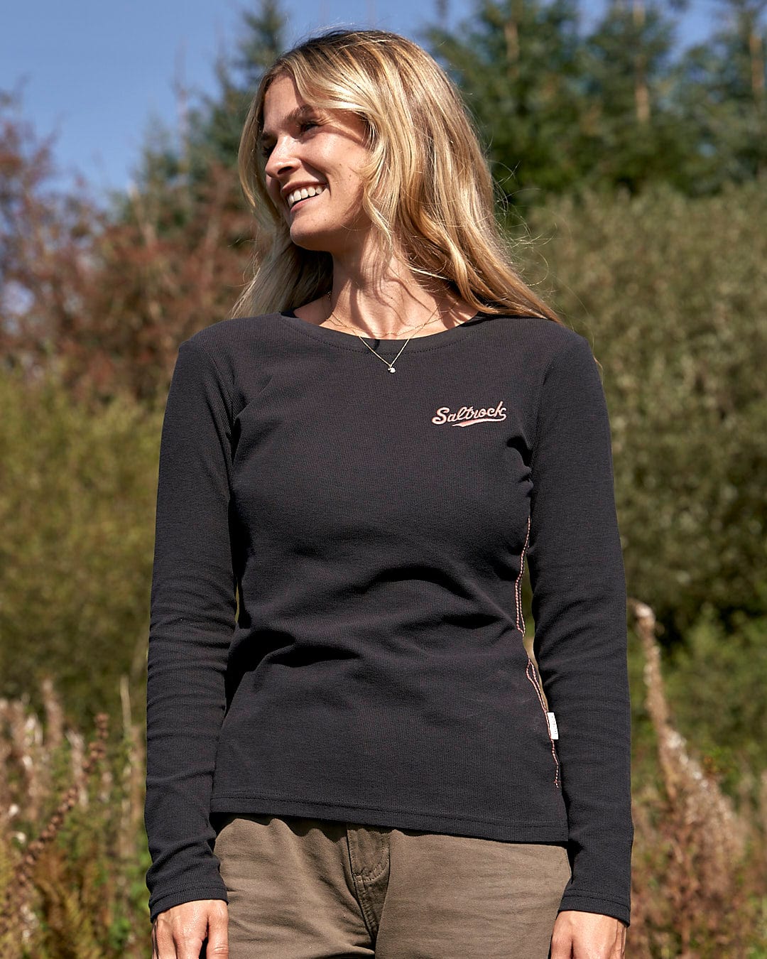 A woman wearing the Saltrock Rory - Womens Long Sleeve Waffle T-Shirt in Black standing in a field.