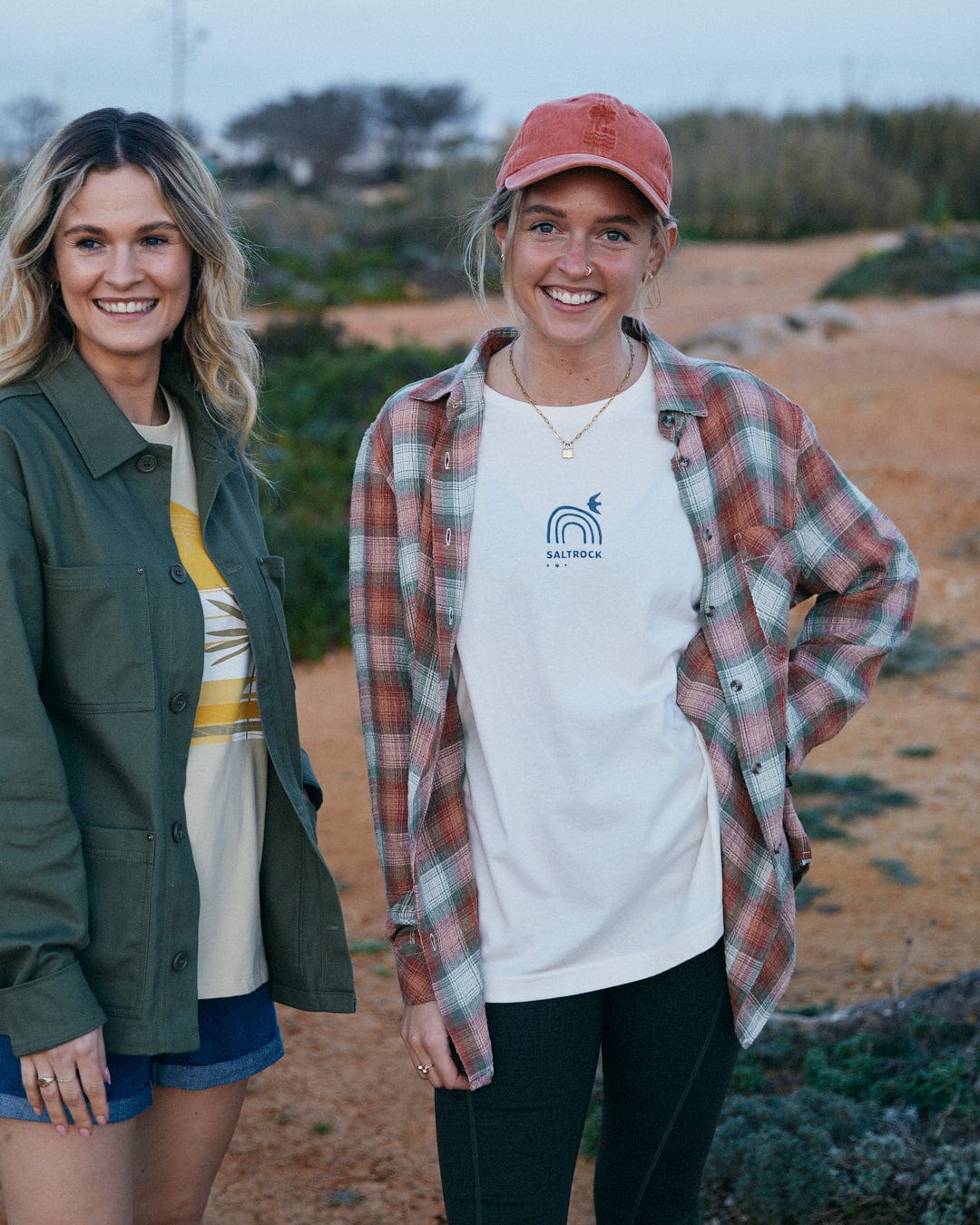 Two smiling women standing outdoors wearing casual clothes with one wearing a cap and the other in a Saltrock Rosalin - Womens Long Sleeve Shirt in Orange/green.