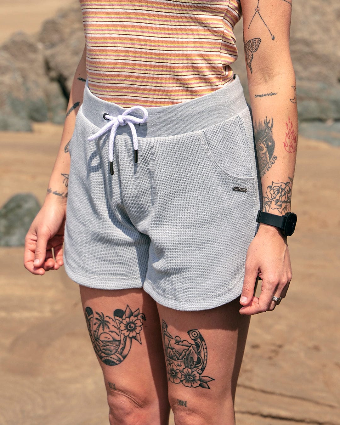 A woman with tattoos standing on a beach wearing Rosalin - Womens Sweat Shorts in Light Grey by Saltrock.