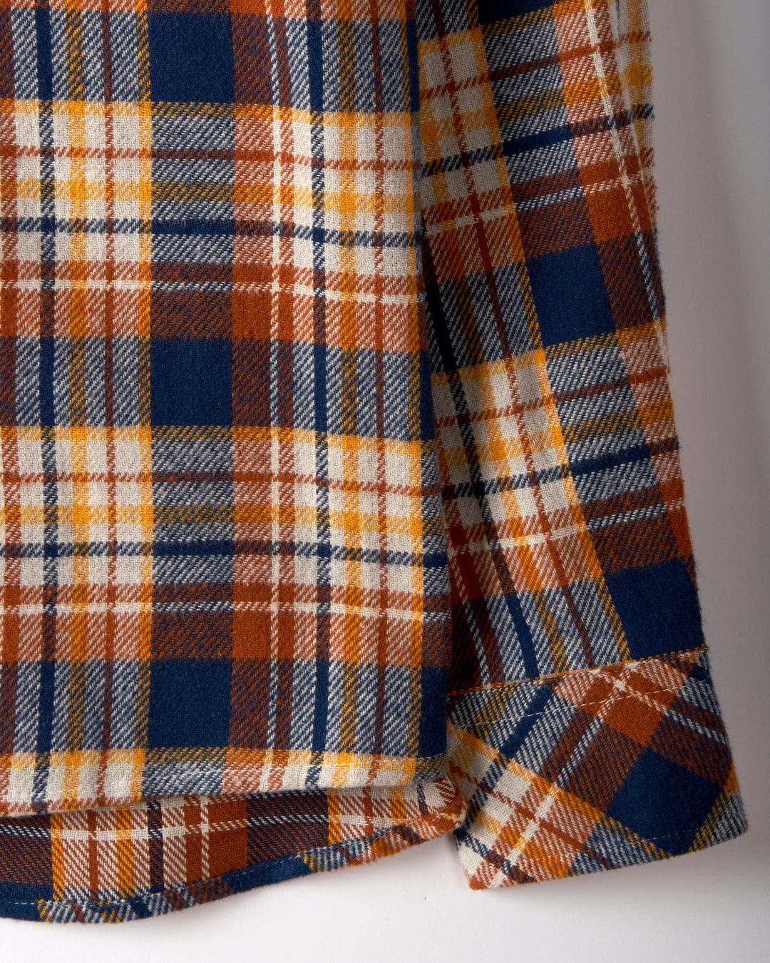 Close-up of the Rosalin by Saltrock, a women's check shirt in burnt orange. It displays blue and white plaid patterns, metallic buttons, and visible hem and sleeve edges that highlight the brushed cotton's texture and design.