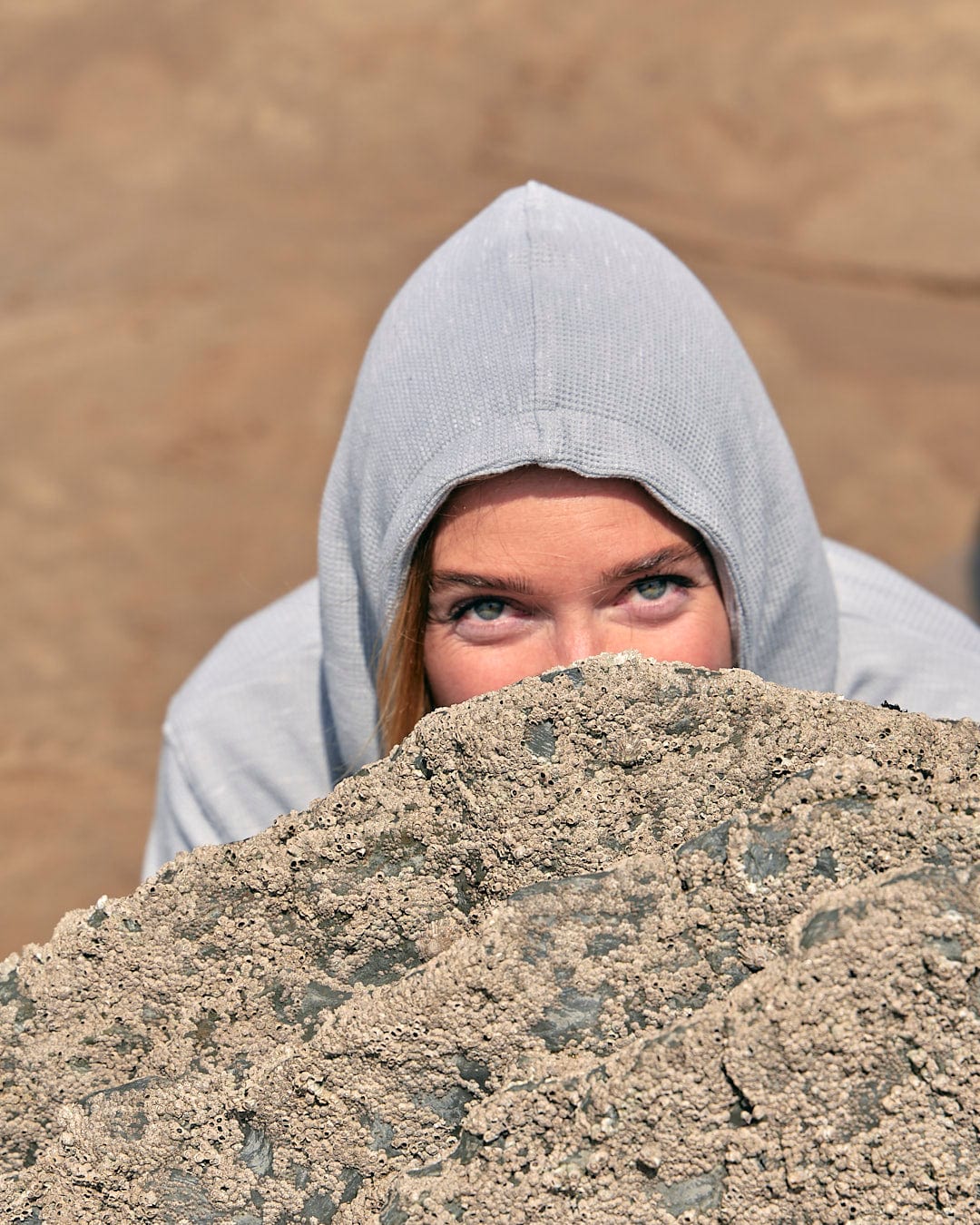 A girl in a Rosalin - Womens Zip Hoodie - Light Grey, made by Saltrock, peeking out of a rock.