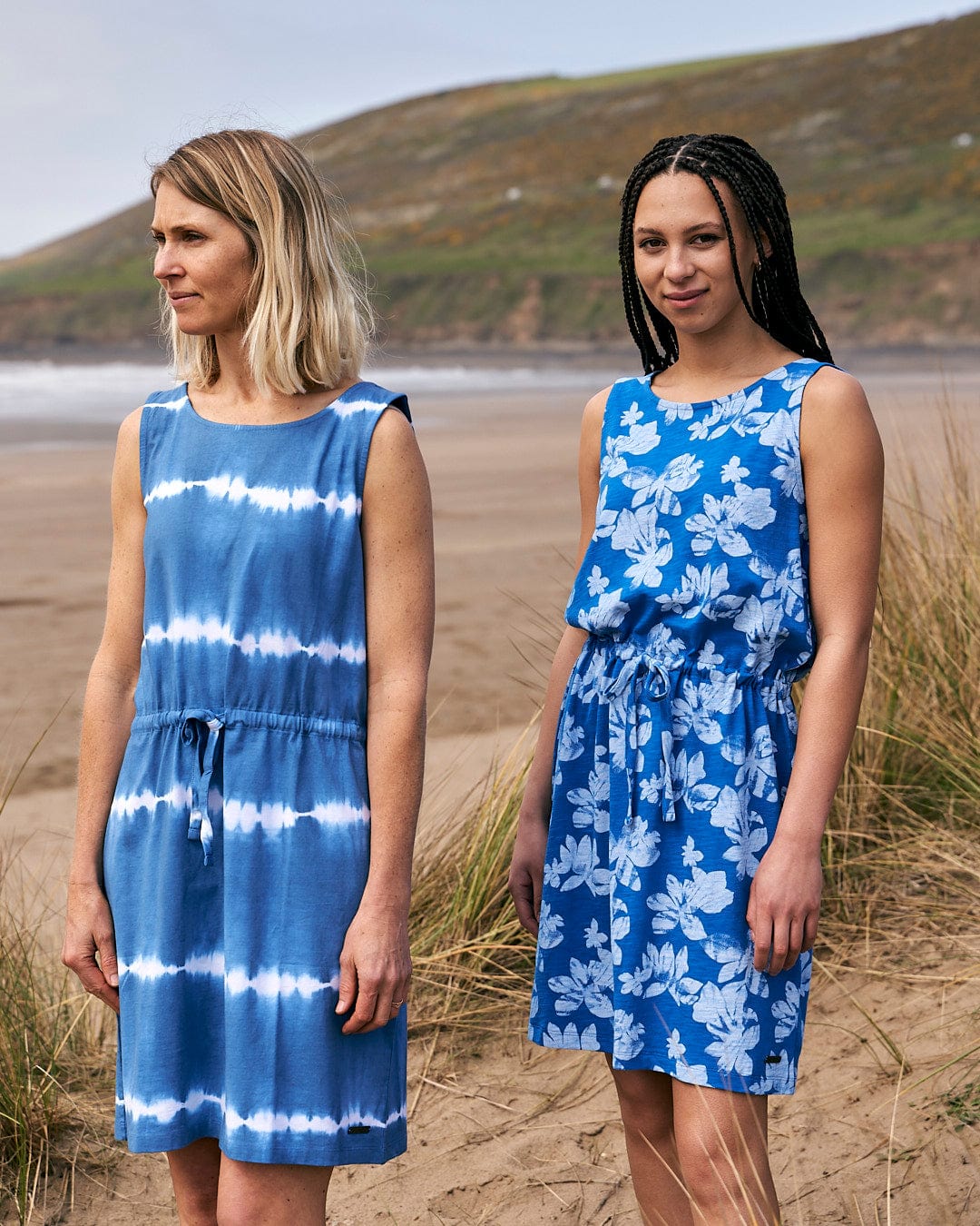 Two women standing next to each other on a beach wearing Saltrock's Floral - Womens Tie Vest Dress in Blue.