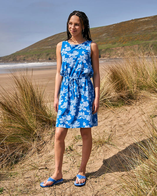 A woman in a Saltrock Floral - Womens Tie Vest Dress - Blue standing on the beach.