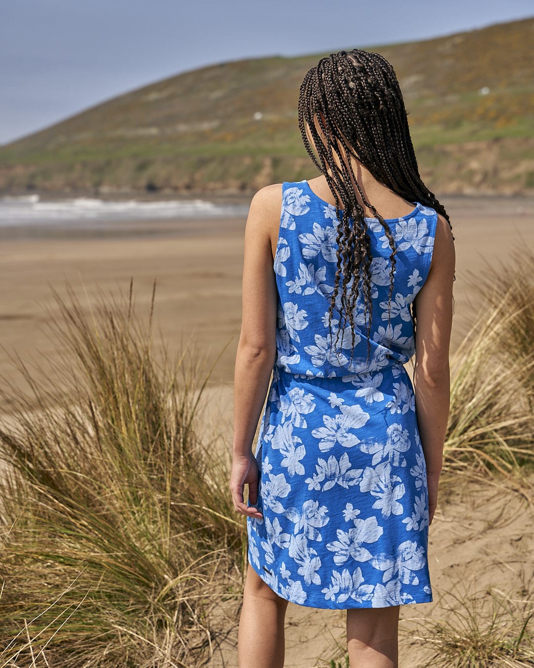 A woman in a Saltrock Floral - Womens Tie Vest Dress - Blue standing on a beach.