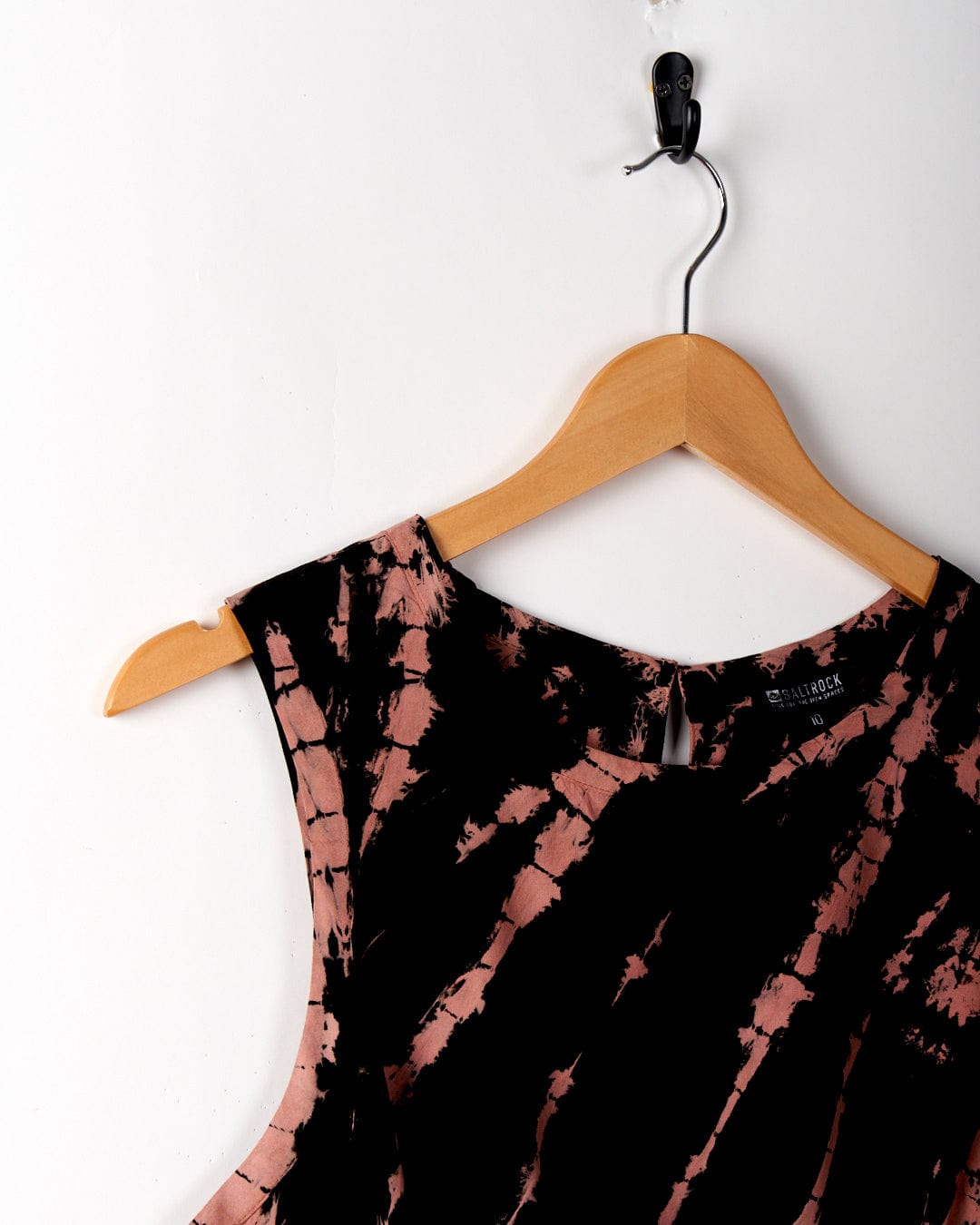 A Saltrock Saffron - Womens Tie Front Vest - Black is hanging on a wooden hanger. The hanger, missing its left shoulder, is hung on a black hook against a white wall. Made from lightweight material, this stylish piece is perfect for any occasion and easy to care for as it’s machine washable.