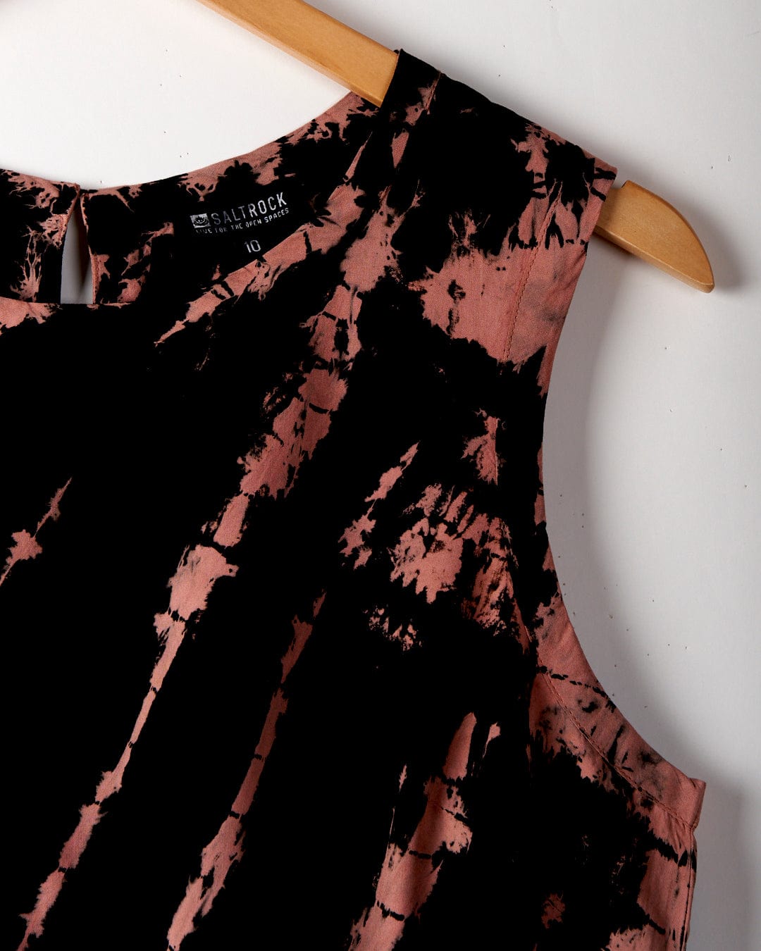 A sleeveless, black and pink tie-dye Saffron - Womens Tie Front Vest - Black made by Saltrock hangs on a wooden hanger.