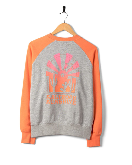 Grey and orange long-sleeved Saltrock Sunshine sweatshirt, featuring raglan sleeves, hanging on a wooden hanger against a white background.