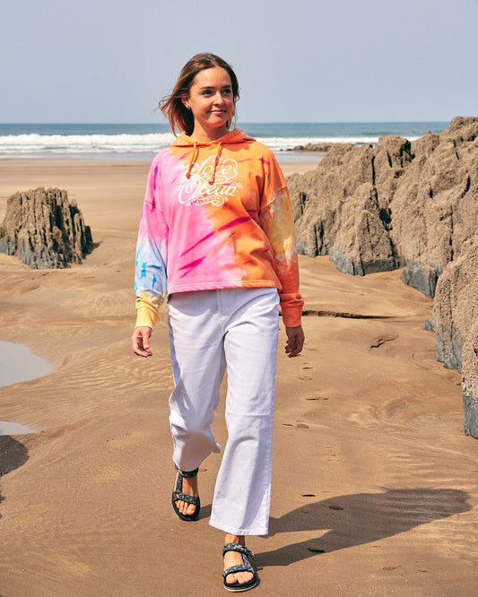 A woman wearing a Samantha - Womens Tie Dye Pop Hoodie - Pink by Saltrock walking on the beach.