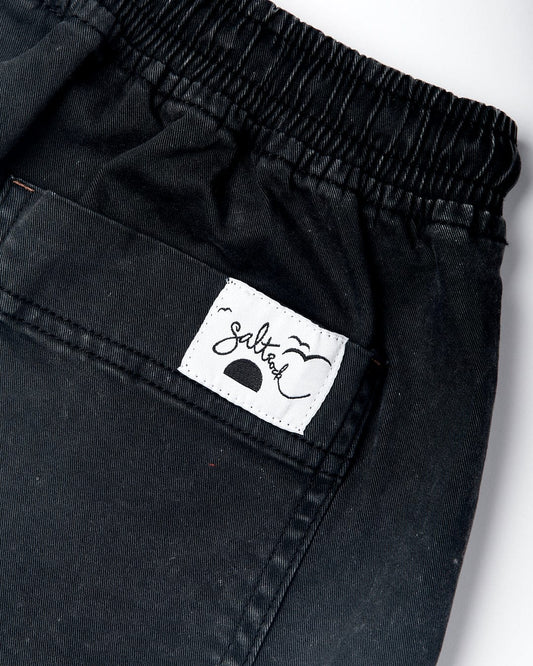 Close-up of a Santano - Womens Short - Washed Black garment with an elasticated waist, featuring a square white label with the word "Saltrock" in a cursive font, stitched on the back.
