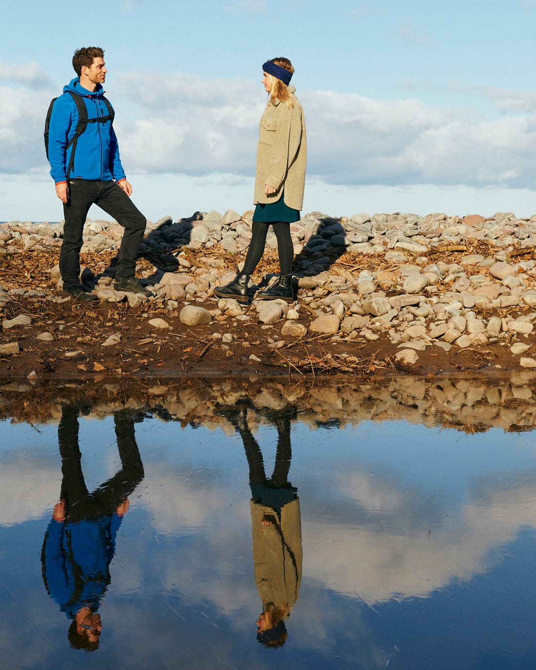 Description: A man and a woman standing next to a pond featuring Saltrock branding, wearing garments made of Senja - Mens Fleece Hoodie - Blue.