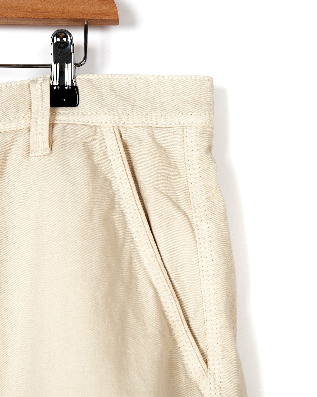 A pair of Sennen - Mens Chino Shorts - Natural hanging on a wooden hanger. (Brand: Saltrock)