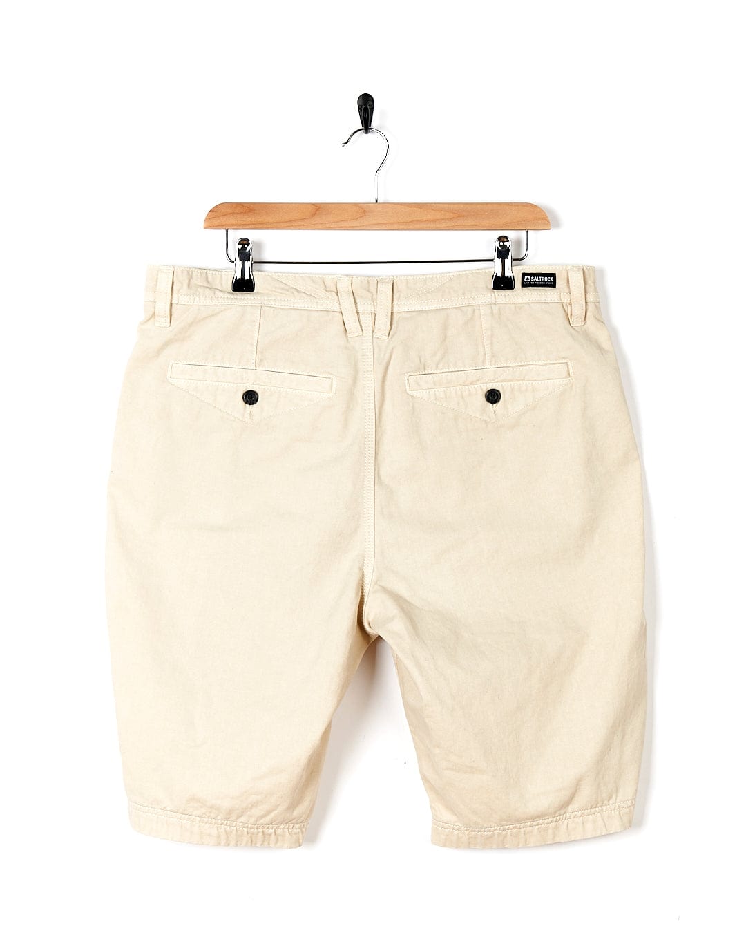 A pair of Sennen - Mens Chino Shorts - Natural by Saltrock hanging on a hanger.