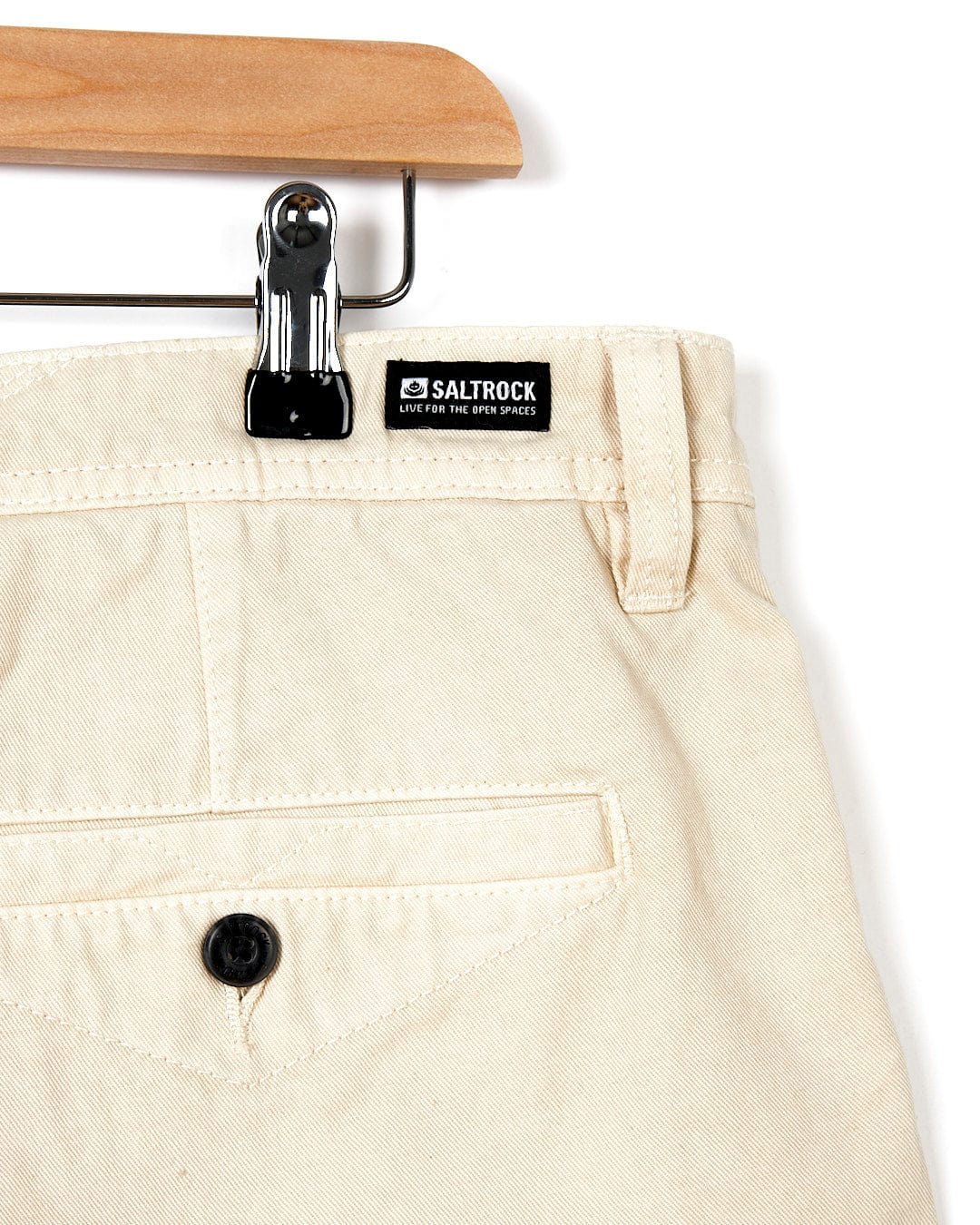 A pair of Sennen - Mens Chino Shorts - Natural hanging on a wooden hanger by Saltrock.