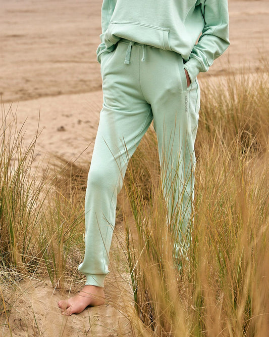 A woman wearing a Saltrock Shelley - Womens Jogger - Light Green sweatshirt and joggers on the beach.