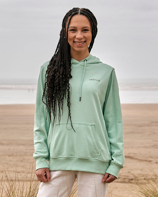 A woman wearing a Shelley - Womens Pop Hoodie - Light Green by Saltrock standing on the beach.