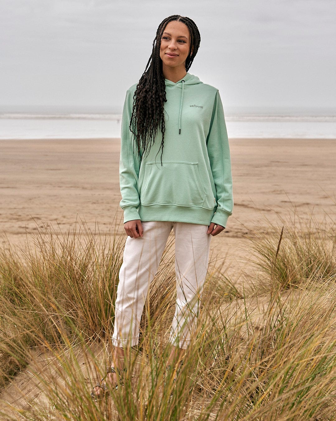 A woman standing on the beach in a Saltrock Shelley - Womens Pop Hoodie - Light Green.