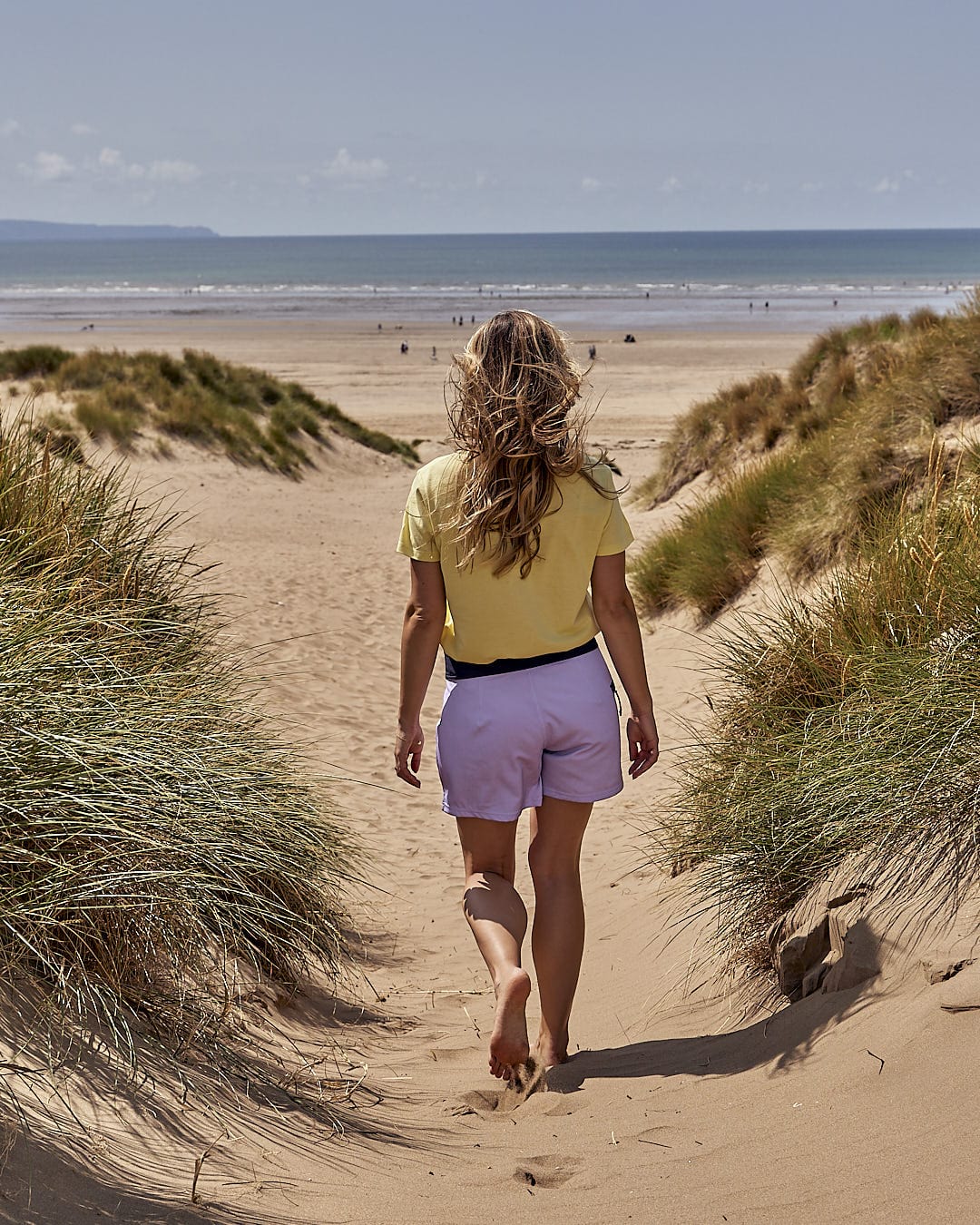 A woman walking on sand wearing the Shoreline - Womens Boardshort - Light Purple by Saltrock.