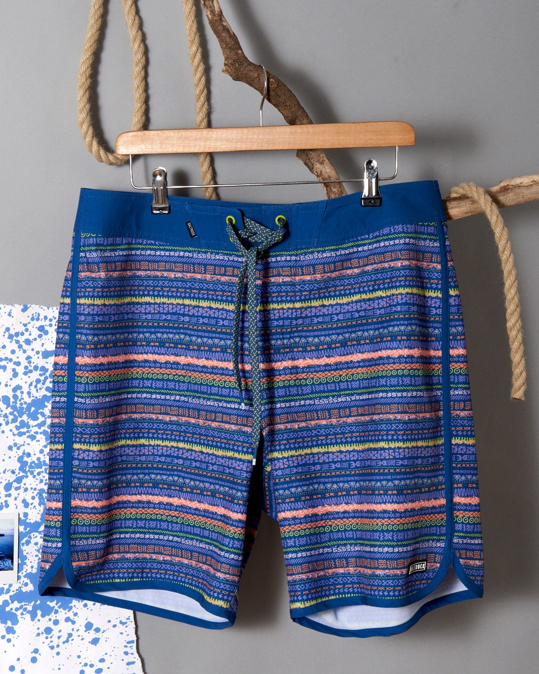 A blue and orange striped Aztec print Saltrock Silas board short hanging on a rope.