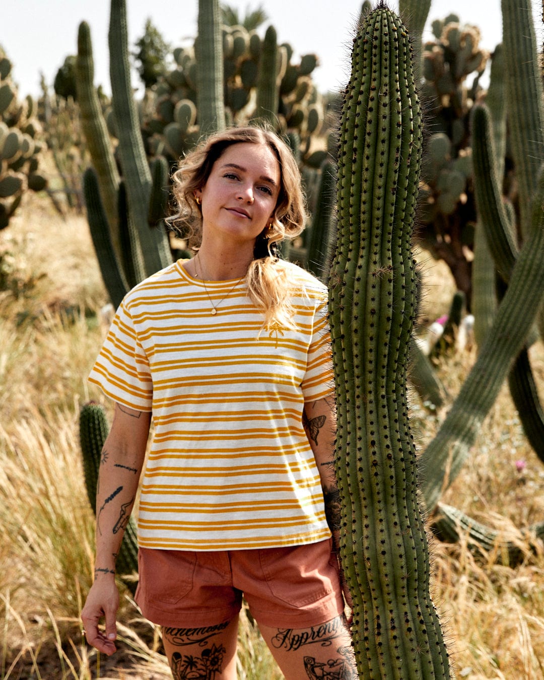 Woman in a striped yellow Saltrock Sky Womens Short Sleeve T-Shirt and orange shorts standing in front of tall cacti.