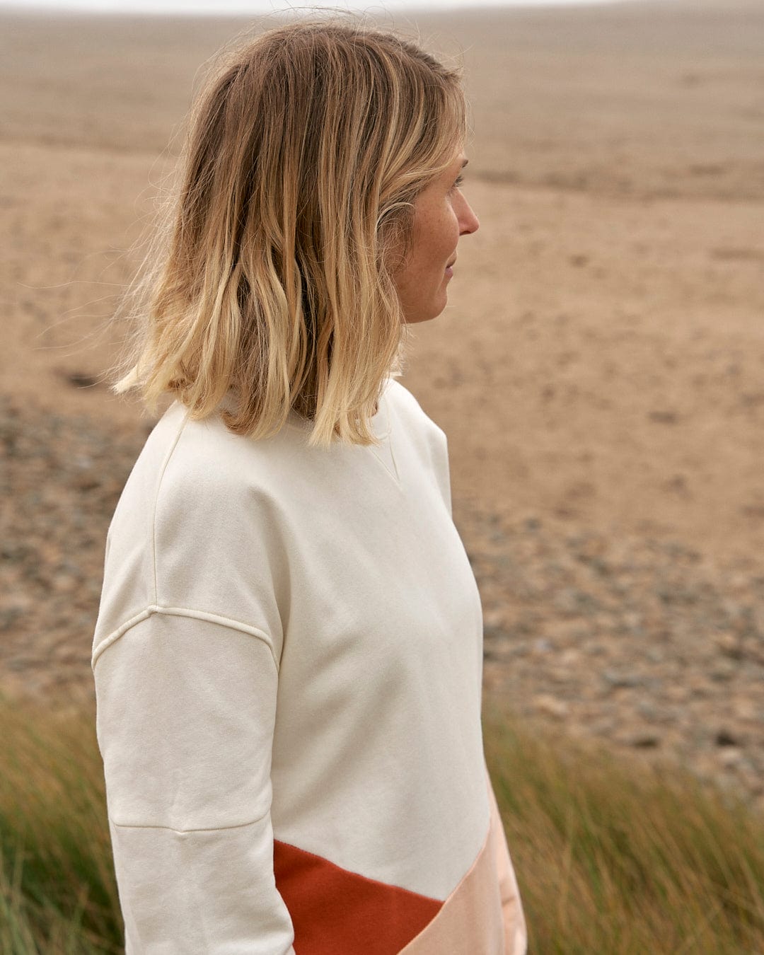 A woman standing in a field wearing a Saltrock Sofie - Womens Boyfriend Fit Sweat - Light Orange/Cream sweater.