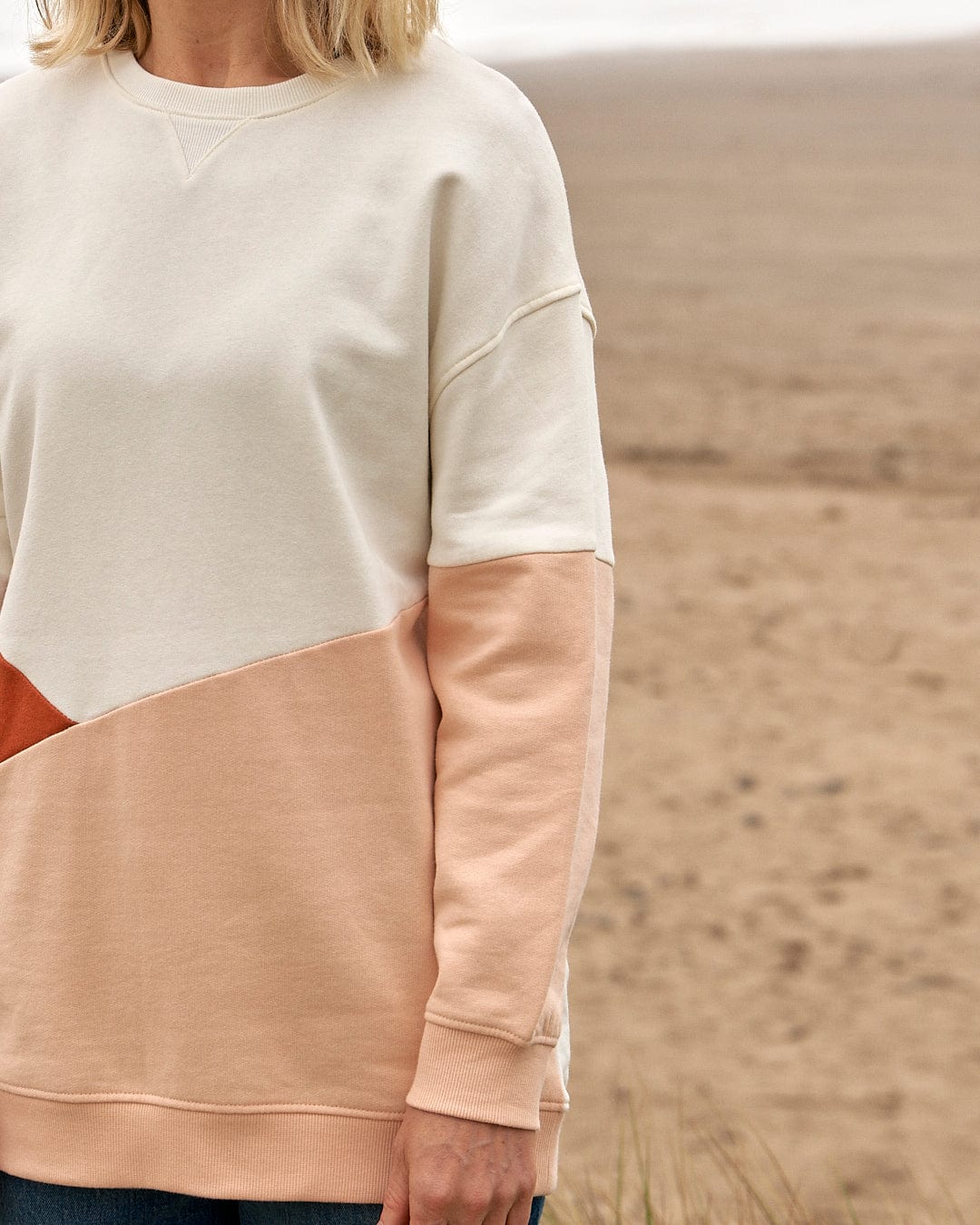 A woman is standing on the beach wearing a Saltrock Sofie - Womens Boyfriend Fit Sweat - Light Orange/Cream sweater.