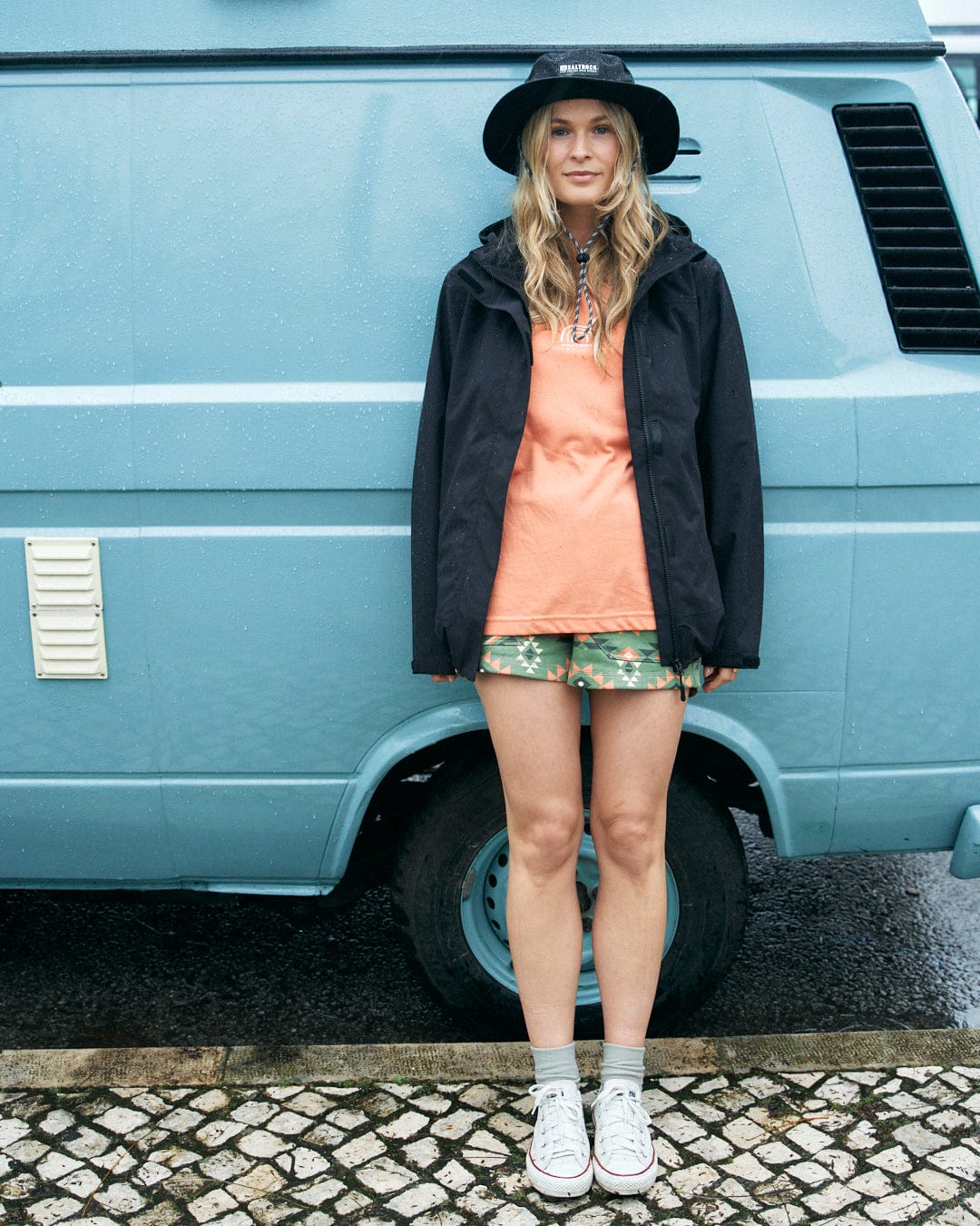 A woman is standing in front of a blue van wearing Saltrock Aztec Santano Womens Sweatshorts in Green/Orange with an elasticated waistband.