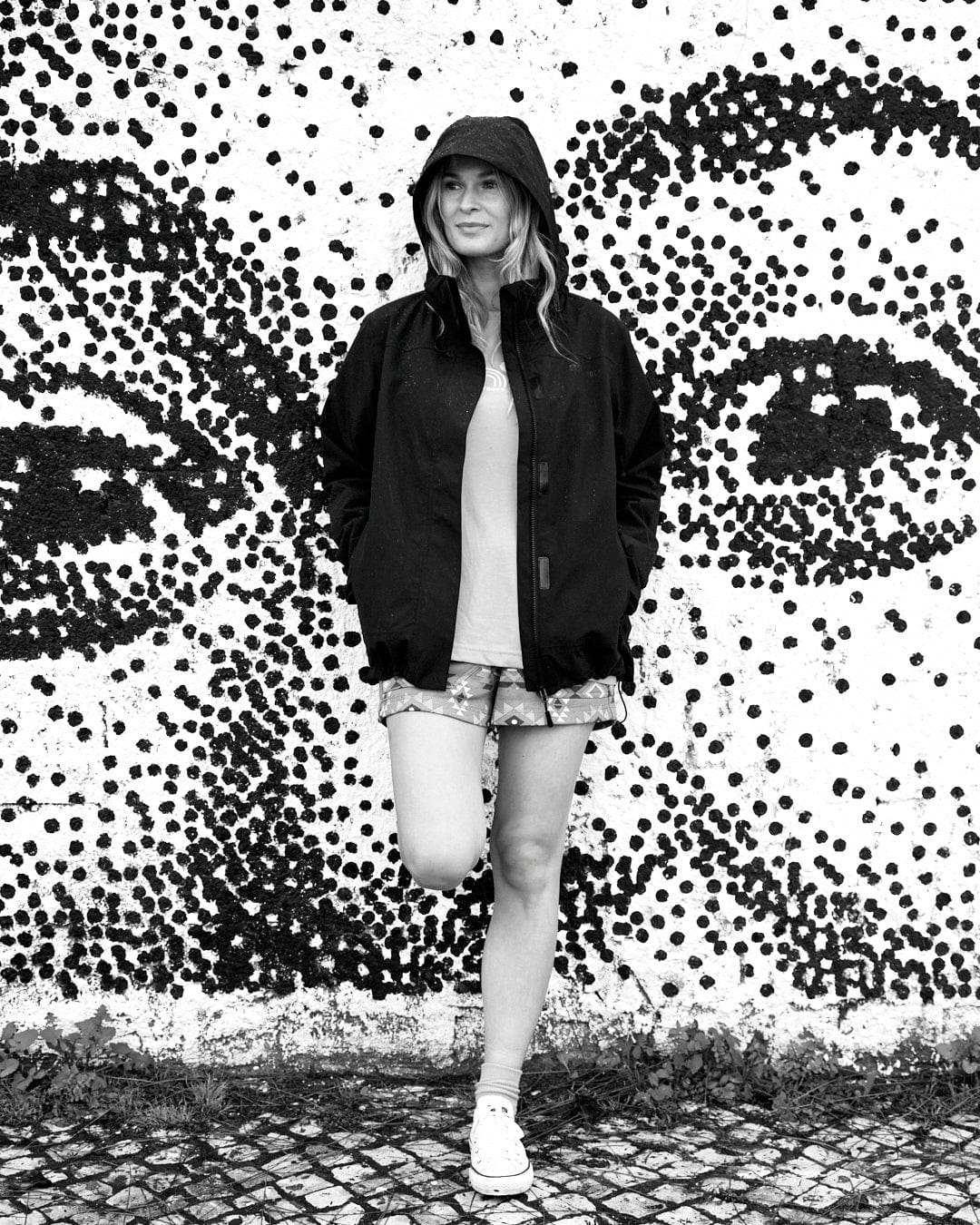 A black and white photo of a woman posing in front of a polka dot wall, showcasing Saltrock's Reflective Solar - Womens Softshell Jacket in Black branding.