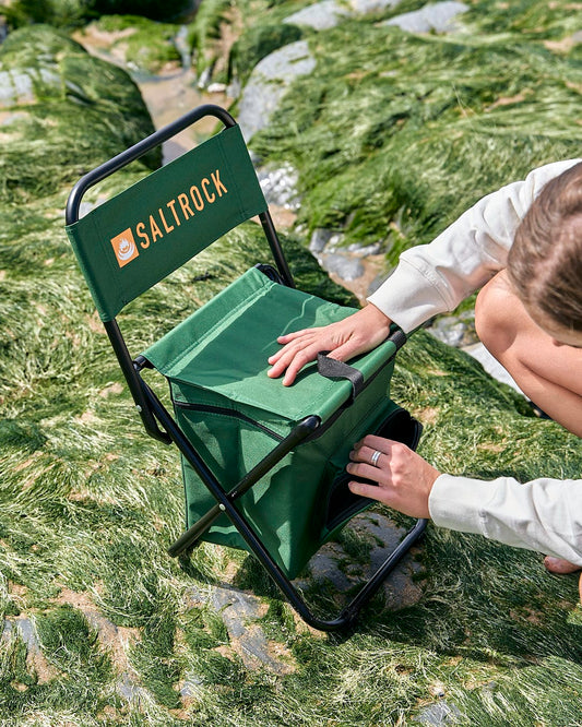A woman is putting a Saltrock Spectator - Foldable Chair with Cooler Bag - Dark Green on the ground.