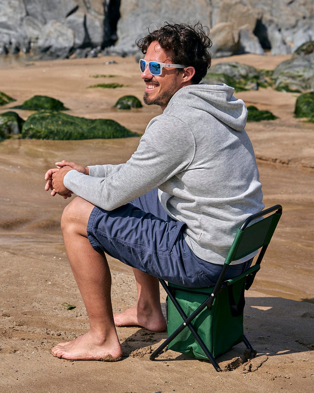 A man sitting on a Saltrock Spectator - Foldable Chair with Cooler Bag - Dark Green on the beach.