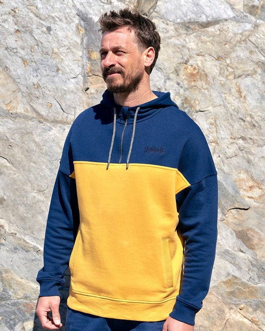 A man wearing a Saltrock Speed Embroidery - Mens 1/4 Neck Zip - Blue/Yellow hoodie.