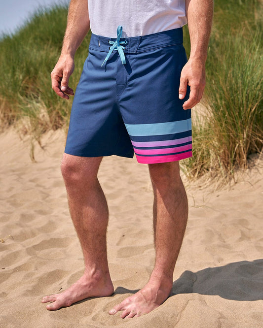 A man is standing on a beach wearing Saltrock's Splash Gradient - Mens Boardshort - Dark Blue.